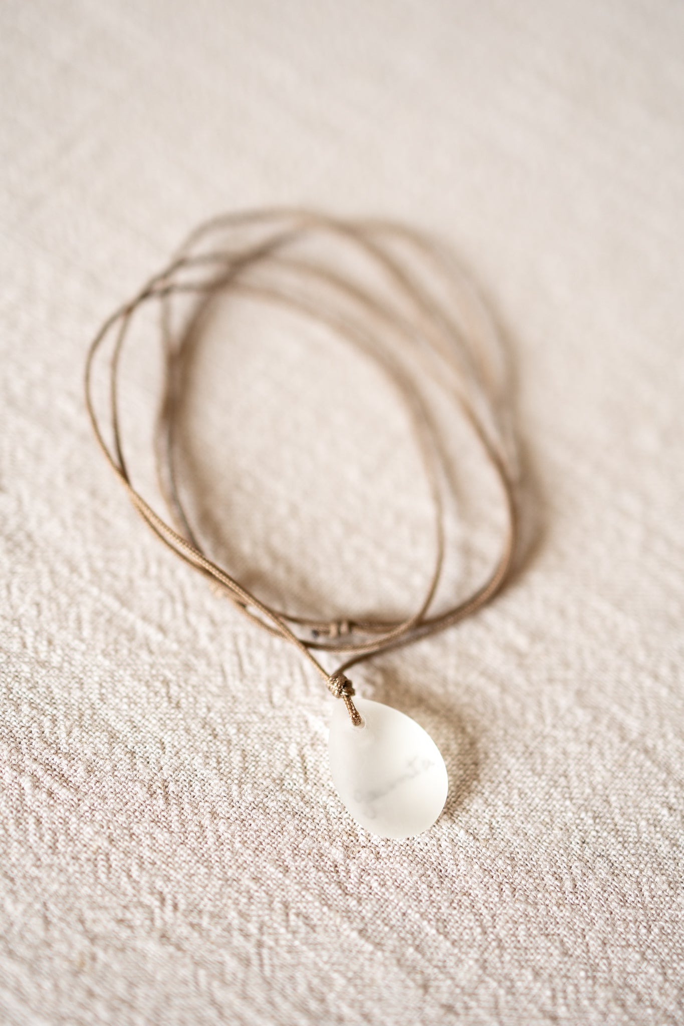 Necklace with a white pendant on a beige fabric background